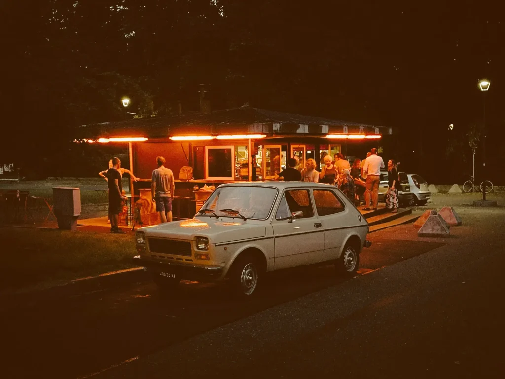 Fiat bij een cafe geparkeerd met. mensen op achtergrond in de avond